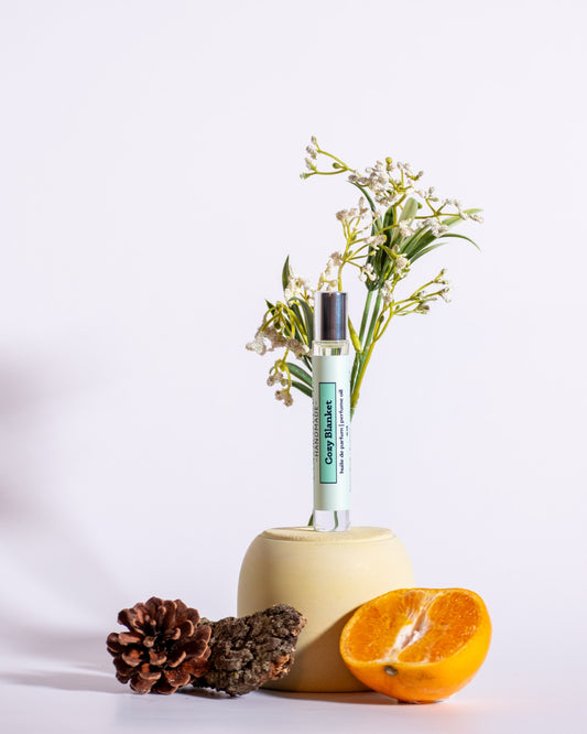Color & Flame Handmade Cozy Blanket perfume oil styled with orange, pine cone, bark, and white flowers.