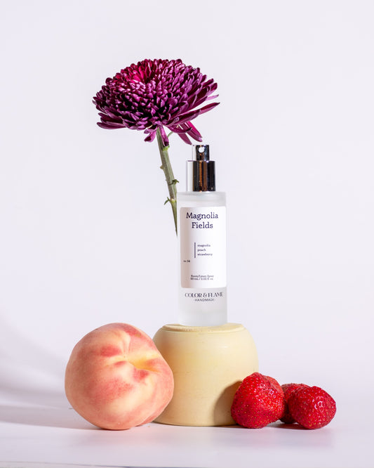 Color & Flame Handmade Magnolia Fields room and linen spray styled with peach, strawberries, and a purple flower.