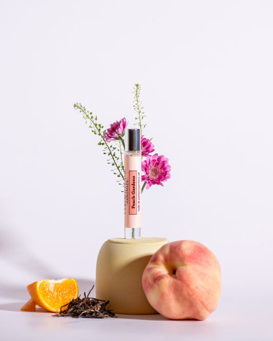 Color & Flame Handmade Peach Gardens perfume oil styled with peach, orange, tea leaves, and pink flowers.