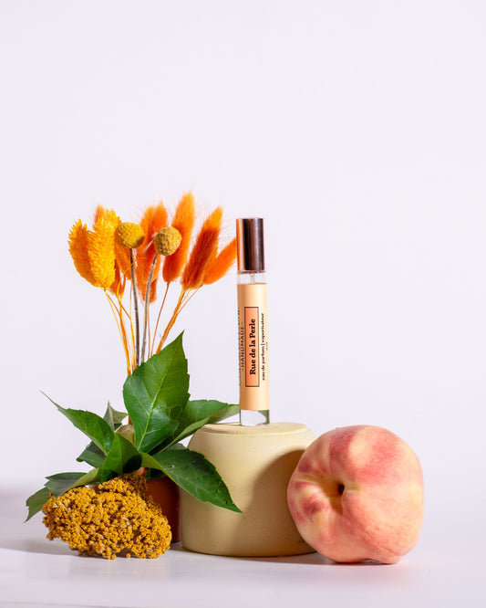 Color & Flame Handmade Rue de la Perle perfume spray styled with peach, green leaves, and warm orange dried botanicals.