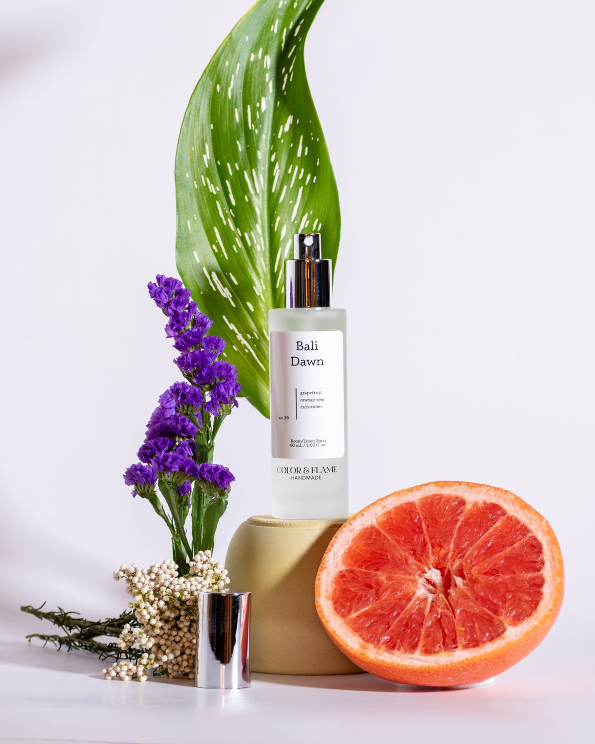Color & Flame Handmade Bali Dawn room and linen spray styled with grapefruit, purple flowers, greenery, and white florals.