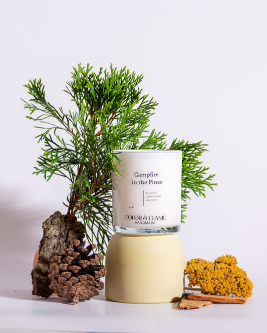 Color & Flame Handmade Campfire in the Pines candle styled with evergreen branches, pine cone, bark, and dried botanicals.

