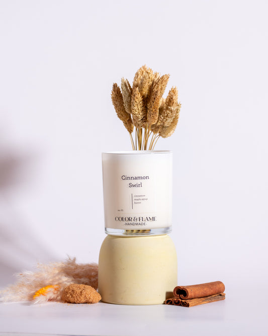 Color & Flame Handmade Cinnamon Swirl candle styled with cinnamon sticks, brown sugar, dried wheat, and warm-toned botanicals.

