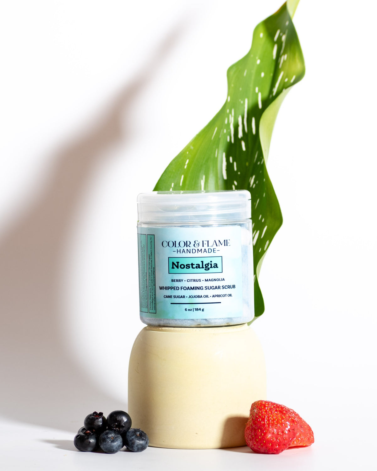 Color & Flame Handmade Nostalgia whipped foaming sugar scrub styled with a green leaf, blueberries, and a strawberry.

