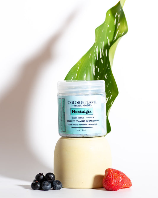 Color & Flame Handmade Nostalgia whipped foaming sugar scrub styled with a green leaf, blueberries, and a strawberry.
