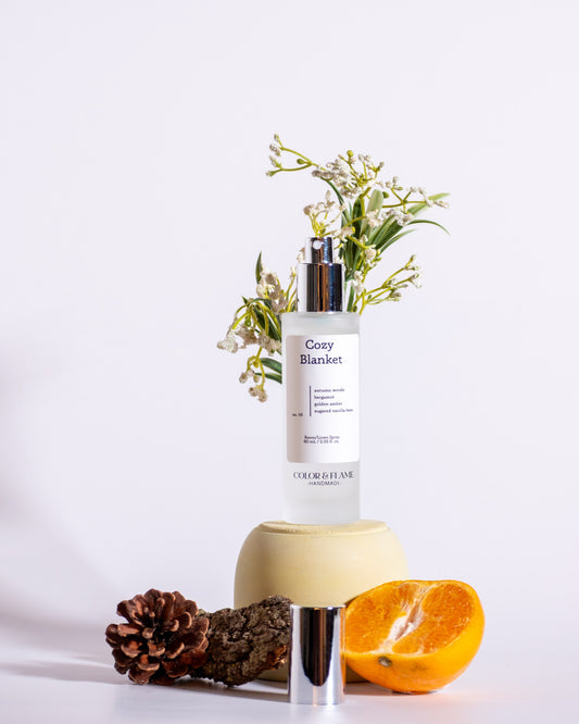 Color & Flame Handmade Cozy Blanket room and linen spray styled with evergreen, pine cone, bark, orange, and white flowers.
