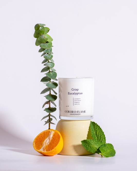 Color & Flame Handmade Crisp Eucalyptus candle styled with eucalyptus, fresh mint leaves, and an orange half.
