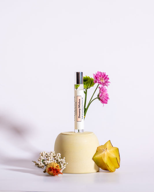 Color & Flame Handmade Dreamy Wishes perfume oil styled with starfruit, pink and green flowers, and white dried botanicals.

