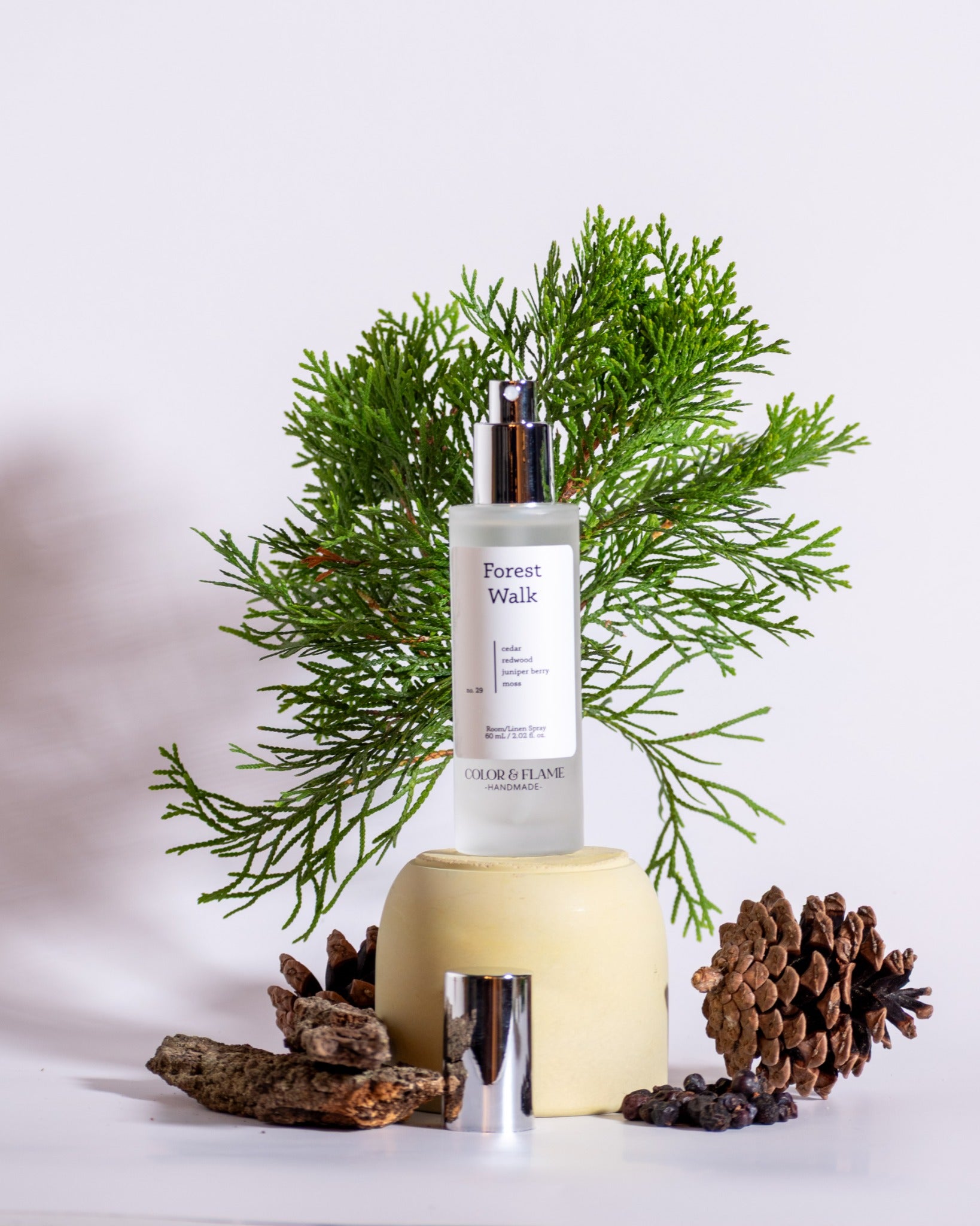 Color & Flame Handmade Forest Walk room and linen spray styled with evergreen branches, pine cone, bark, and dark berries.
