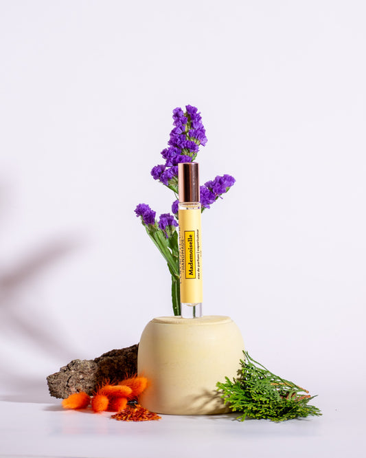 Color & Flame Handmade Mademoiselle perfume spray styled with purple flowers, evergreen branches, bark, and orange dried botanicals.
