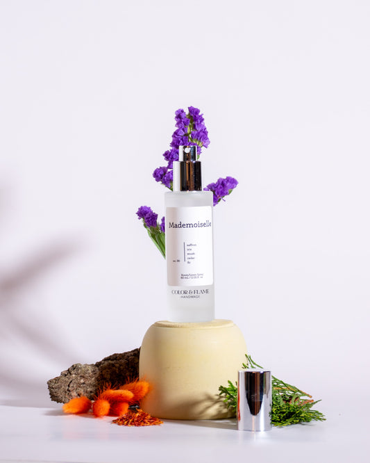 Color & Flame Handmade Mademoiselle room and linen spray styled with purple flowers, evergreen, bark, and orange dried florals.
