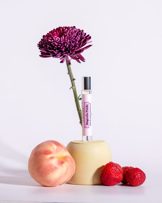 Color & Flame Handmade Magnolia Fields perfume oil styled with peach, strawberries, and a deep purple flower.
