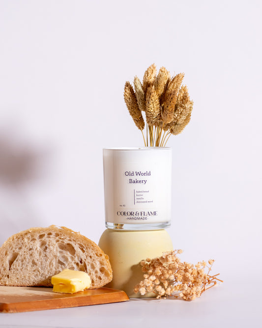 Color & Flame Handmade Old World Bakery candle styled with rustic bread, butter, wheat, and dried white flowers.
