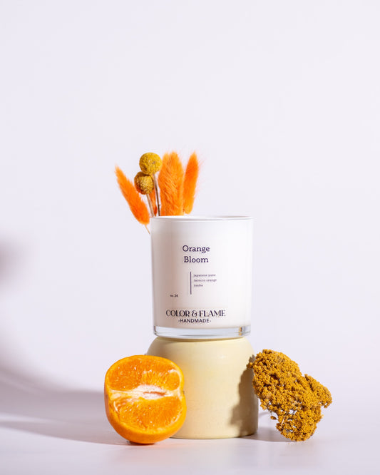 Color & Flame Handmade Orange Bloom candle styled with a fresh orange half and warm yellow and orange dried botanicals.
