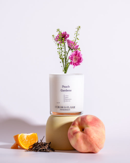 Color & Flame Handmade Peach Gardens candle styled with a peach, orange, loose tea leaves, and pink flowers.
