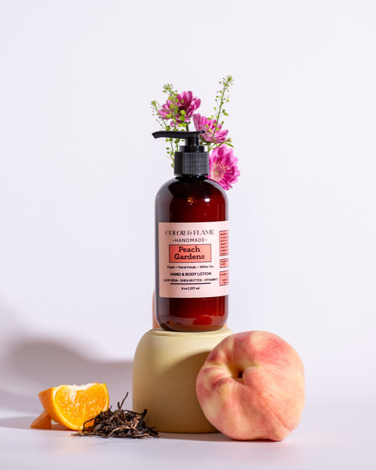 Color & Flame Handmade Peach Gardens hand and body lotion styled with peach, orange, tea leaves, and pink flowers.
