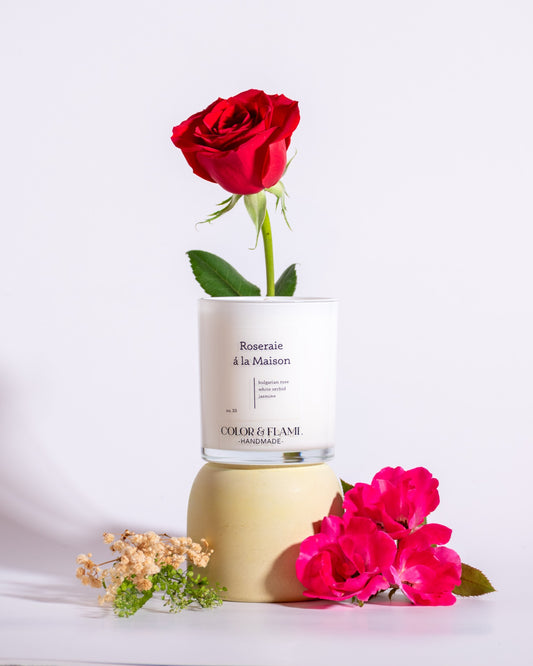 Color & Flame Handmade Roseraie à la Maison candle styled with a red rose, pink roses, dried petals, and natural wood.
