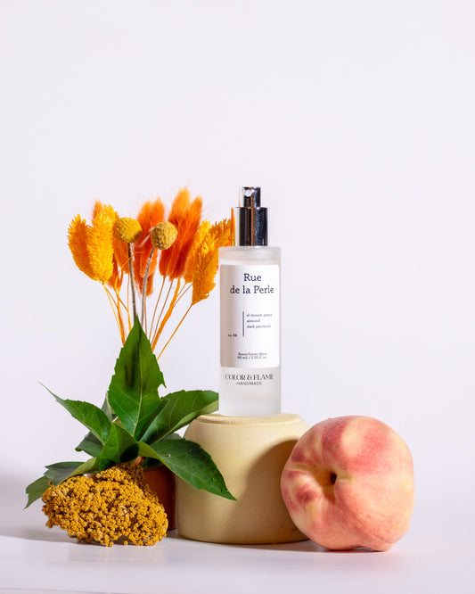 Color & Flame Handmade Rue de la Perle room and linen spray styled with peach, green leaves, and golden dried flowers.
