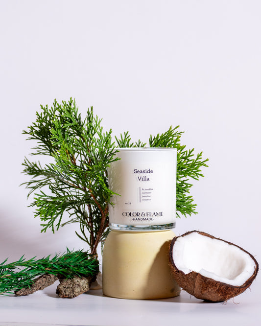 Color & Flame Handmade Seaside Villa candle styled with coconut, evergreen branches, bark, and coastal-inspired greenery.
